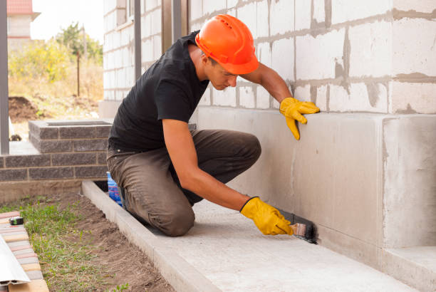 Worker applying waterproofing sealant to a foundation wall