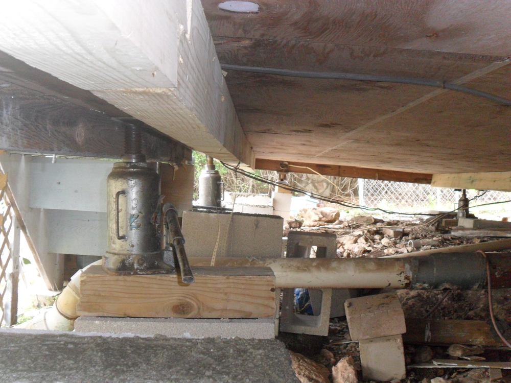 Hydraulic jack lifting a house foundation for leveling and stabilization